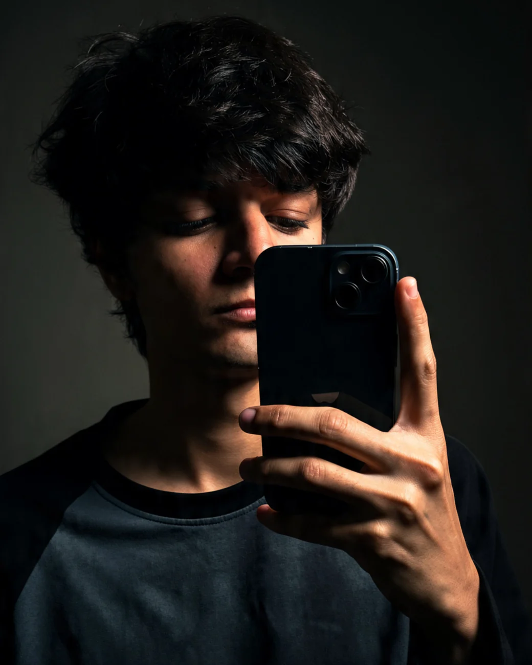 Portrait of Nishad Suthar holding a phone, softly lit against a dark background